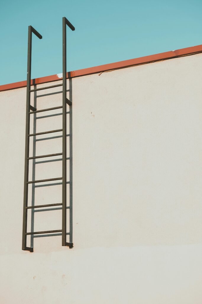 Minimalist view of a metal ladder mounted on a rooftop with a clear blue sky background.