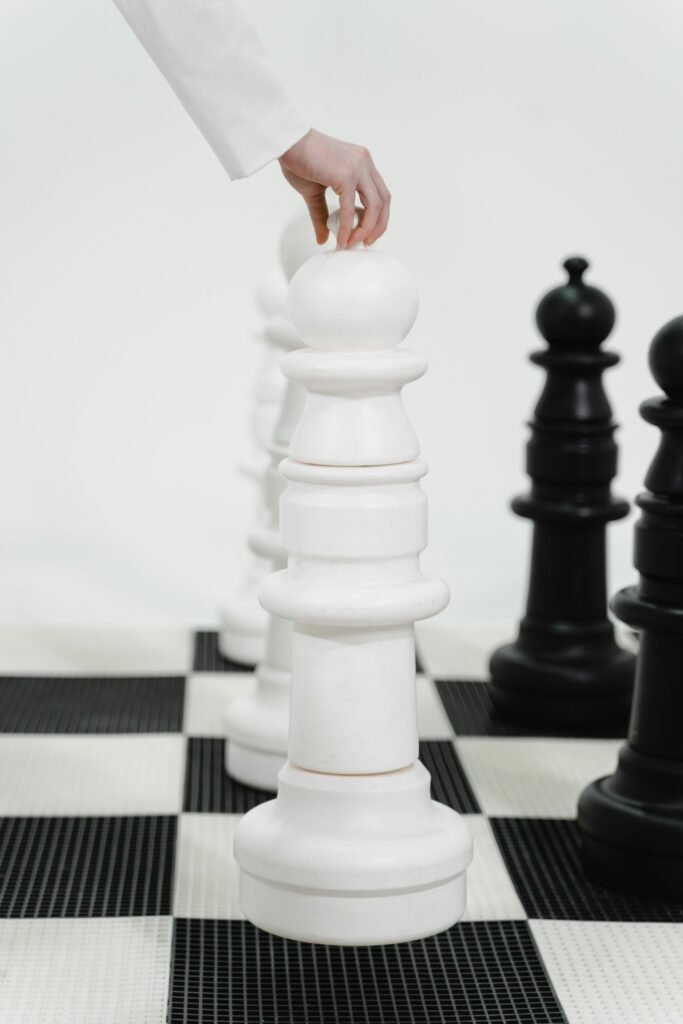 Close-up of a hand moving a giant chess piece on a chessboard, symbolizing strategy and competition.